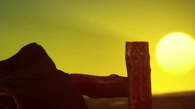 A sunset shows vibrant colors in the sky behind a wooden fence. The outlines of rocks and hills create a simple scene. The setting sun lights the horizon vividly.
