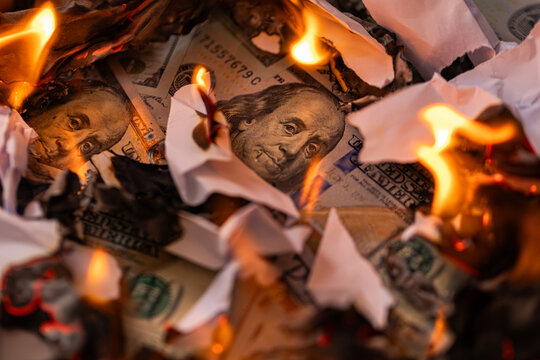 US one hundred dollar bills burning in fire surrounded by ash and flames close up