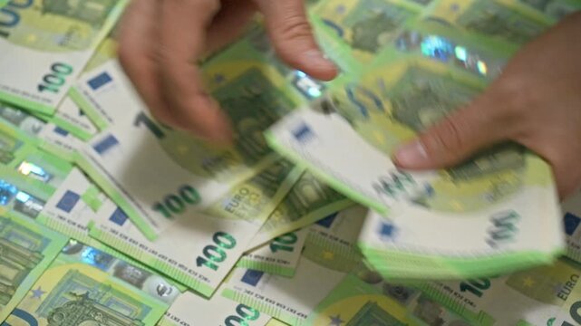 Closeup footage of hands counting a stack of 100 euro banknotes and piling them up