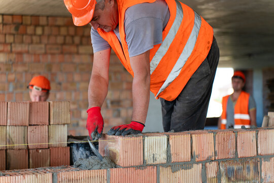 Specialist applies mortar to surface of brick wall. Builder prepares construction for improvement connecting components in work site