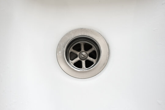 Top down view of a clean chrome drain plug hole in a white ceramic sink basin showing plumbing details