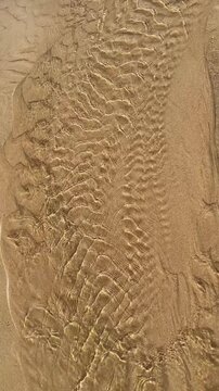 Clear water flows gently over rippled sand, shimmering in the sunlight and revealing natural textures beneath the surface.