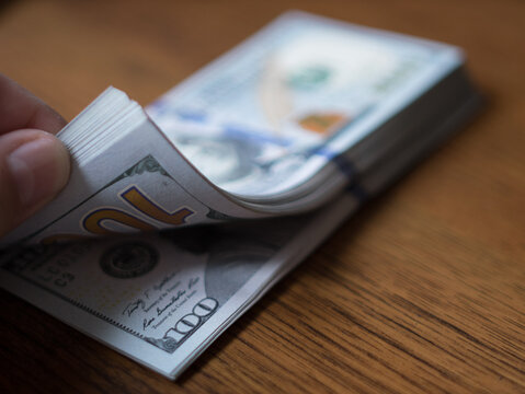 Counting a Stack of 100 Dollar Bills on a Wooden Table
