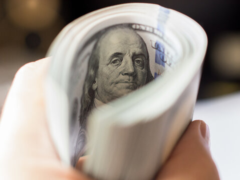 Hand Holding Rolled Stack of One Hundred Dollar Bills