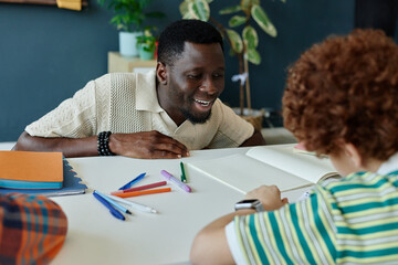 Fototapeta na wymiar Medium shot of Black male teacher guiding schoolboy during writing practice at desk, supporting literacy and learning. Useful for education, tutoring, child development campaigns