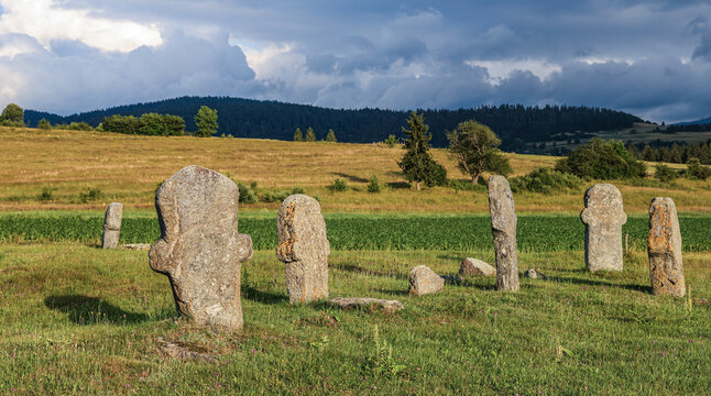 Group of anthropomorphic stone monuments at Maculje Necropolis near Novi Travnik, Bosnia and Herzegovina, standing in a rural landscape beneath dramatic storm clouds.