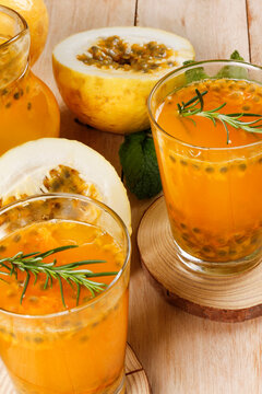 Two glasses of fresh passion fruit juice served with passion fruit slices and aromatic herbs on a rustic wooden table