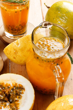Glass pitcher of fresh passion fruit juice, surrounded by whole and sliced ​​tropical fruits on a rustic wooden surface