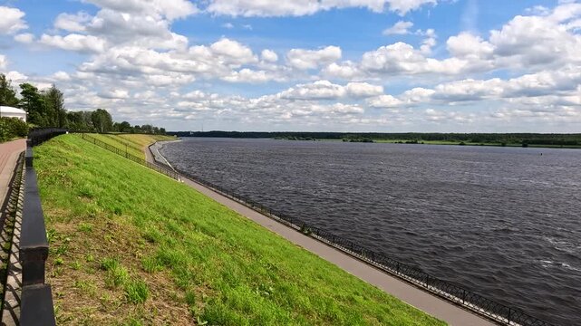 A riverbank with a paved walking path and a blue sky.
