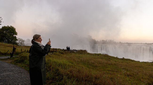 woman taking pictures  of Victoria Falls at sunrise from the Zimbabwe side, Zimbabwe, Africa