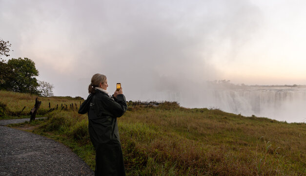 woman taking pictures  of Victoria Falls at sunrise from the Zimbabwe side, Zimbabwe, Africa