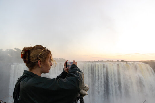 young woman photographing  at Victoria Falls at sunrise from the Zimbabwe side