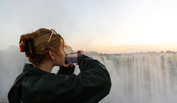 young woman photographing  at Victoria Falls at sunrise from the Zimbabwe side