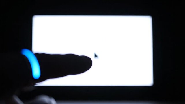A finger wearing a glowing blue smart ring controls a cursor on a white screen in a dark setting, demonstrating futuristic touchless technology and interactive motion control.