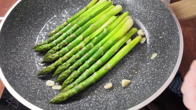 Fresh green asparagus spears sauteing in a nonstick skillet with garlic, close up kitchen cooking scene, healthy vegetable side dish with simple preparation
