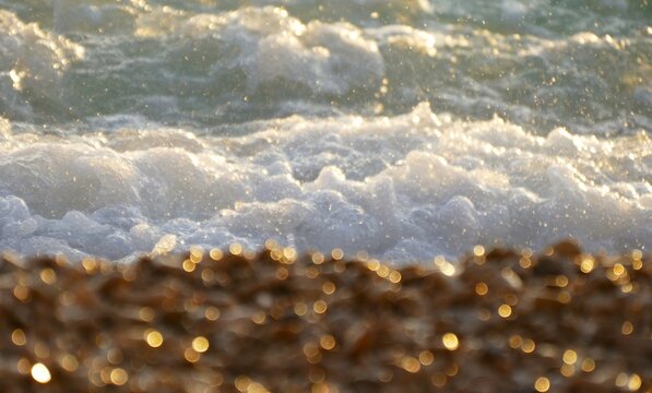 Big waves crushing on the beach with golden sparkling pebbles and foam summer wave splash background