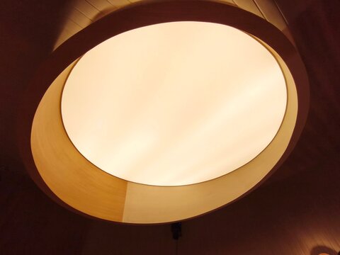 Interior large oval circular ceiling lamp design with warm illumination and minimalist wooden frame.