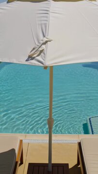Vertical video: Camera pulling back, revealing large white umbrella at pool showing seam and strap
