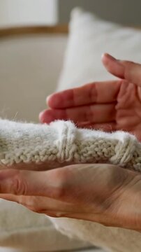Vertical video: Lifting hands smoothing folded cream knit on couch cushion, checking feel and ring