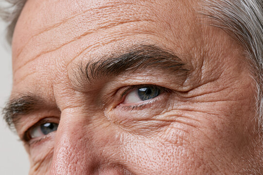 Elderly man skin close up wrinkles crow feet blue eye gray hair mature male cheek texture visible pores expressive gaze