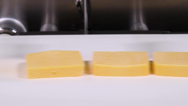 Conveyor belt with pieces of yellow cheese moving on it.