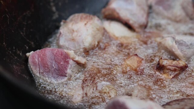 Meat chunks frying in hot oil inside a large wok. Professional cook preparing raw beef for traditional dish. Culinary process of searing food in saucepan pan.