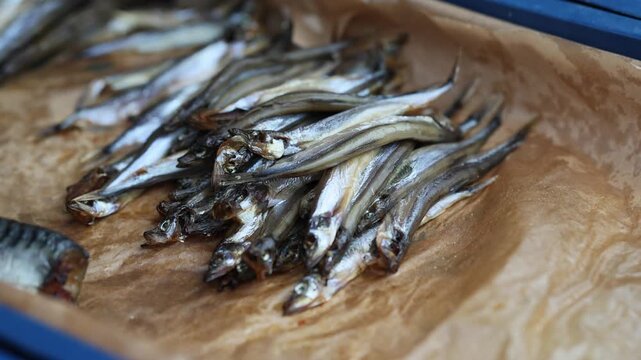 Fried smelts in paper box. Small silver fish prepared for snack or meal. Seafood culinary delicacy displayed in container for sale at local food street market.