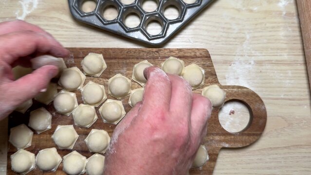 Hands forming homemade dumplings on wooden board, close view of dough rounds and sealed edges, cozy kitchen prep mood, traditional cooking process