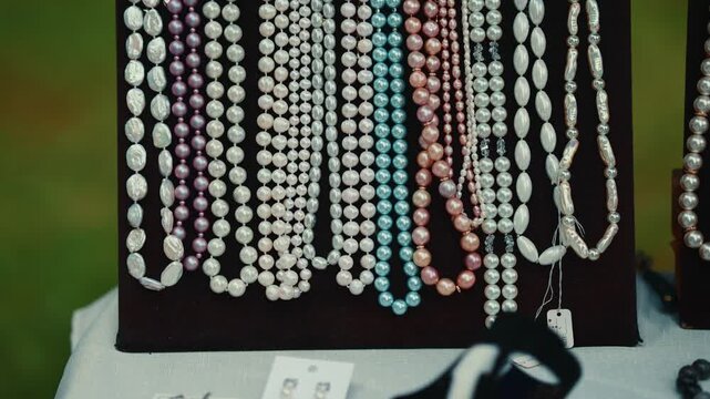 Assortment of pearl necklaces displayed on a velvet jewelry stand. Collection of various bead strings for sale at outdoor market. Decorative accessory retail.