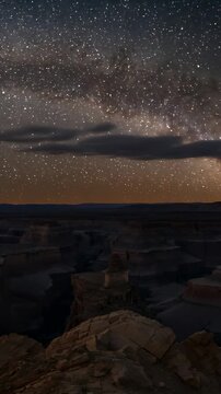 Vertical video: Drifting cloudlets entering frame and crossing Milky Way above rocky canyon rim