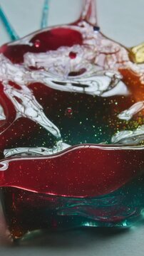 Vertical video: Dropping pipette hitting viscous color pool on white sheet, sending drops outward