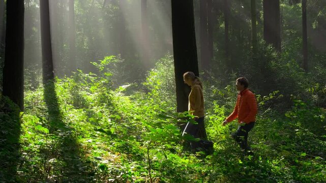 Two hikers in a green forest stopping to watch the beautiful majestic sunbeams in the mist