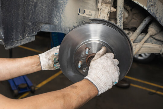 Auto mechanic hands in gloves installing new brake disc on car hub at service station closeup