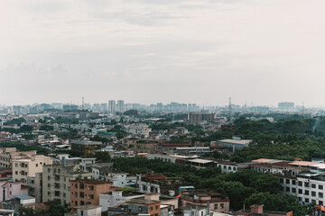 Obraz premium Aerial cityscape view of dense urban neighborhood with mid-rise buildings, green trees, and distant skyline under overcast sky