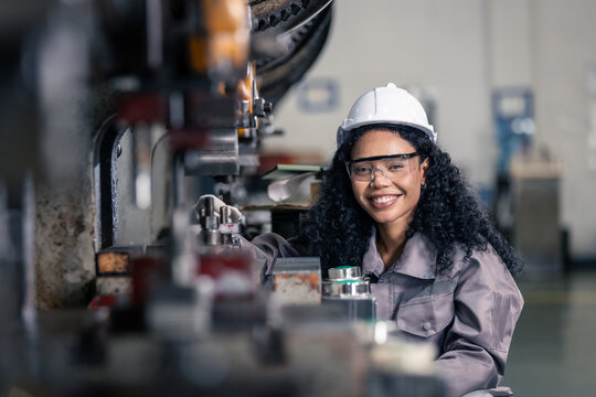 Confident female manufacturing engineer smiling while operating an industrial press machine in a modern factory.