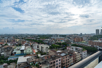Obraz premium Cityscape view from high-rise balcony overlooking dense urban neighborhood under bright blue sky with scattered cumulus clouds
