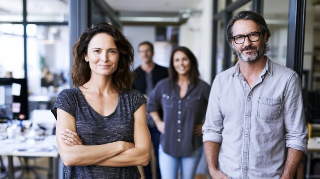 Confident man and woman standing together in modern office with two colleagues in background creating diverse creative team environment