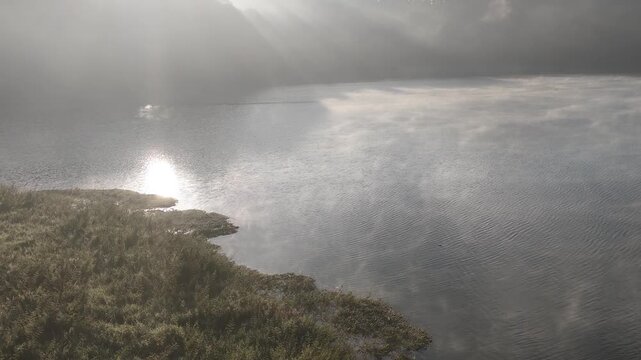 Beautiful cinematic footage of misty Tuyen Lam Lake covered in thick fog during morning sunlight in Dalat, Central Highlands, Vietnam. A serene nature landscape with sun rays reflecting on the water