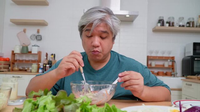 Asian elderly man preparing salad in kitchen, representing healthy food, wellness, nutrition, and lifestyle concept in cheerful indoor environment with vegetables, natural daylight, and positive