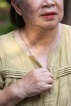 senior asian woman sweating heavily in summer park, embarrassed by stinking cloth and body odor from hot weather, hand waving her dress to ventilate, closeup shot