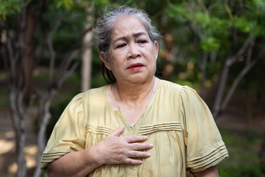 Elderly asian senior woman feels tired, flushing and sweating from excessive outdoors tropical summer heat, having breathing difficulty or shortness of breath due to prolonged dehydration