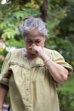 elderly asian female with sweat stains on her dress, feeling uncomfortable with unpleasant smell in a daytime park during hot summer