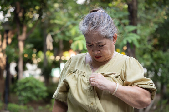elderly asian female with sweat stains on her dress, feeling uncomfortable with unpleasant smell in a daytime park during hot summer