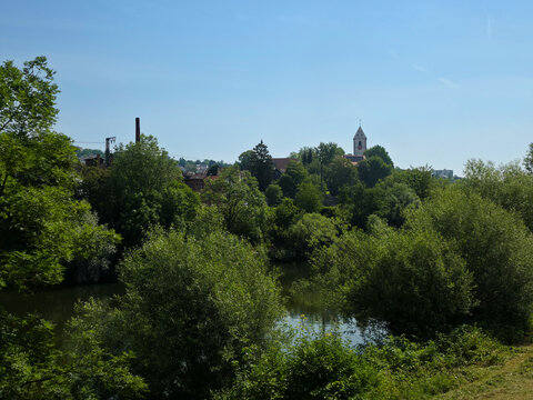 germany, elegant st blasius church steeple overlooking neckar river with lush trees beneath vibrant blue summer sky in plochingen landscape