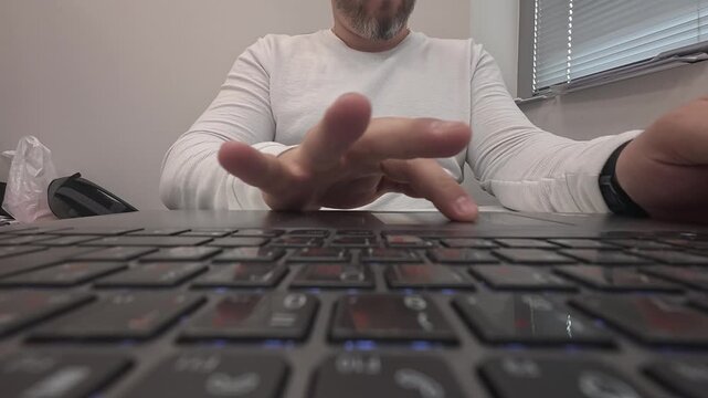 A man's hands are typing efficiently on a laptop keyboard. The footage captures the precise finger movements, the tactile texture of the keys, and the focused rhythm of work. The soft lighting and sha