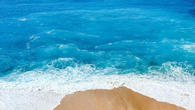 Aerial view of turquoise ocean waves washing onto a sandy beach, bright tropical colors and clean textures, calm summer travel mood