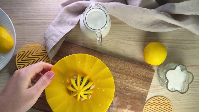 Overhead view of hands preparing lemon dessert on a wooden board with yellow plate and fresh lemons nearby, bright kitchen scene suggesting homemade baking and summer refreshment