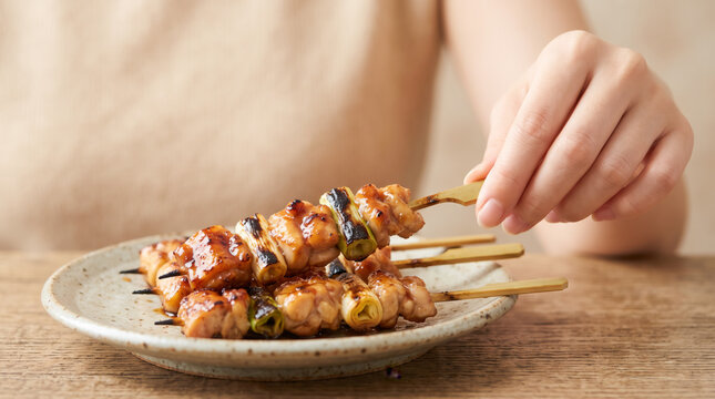 焼き鳥を手に取る手元のクローズアップ タレの掛かったねぎまのやきとり