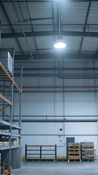 Vertical video: Starting camera moving down center aisle at warehouse, showing pallet racks, lights