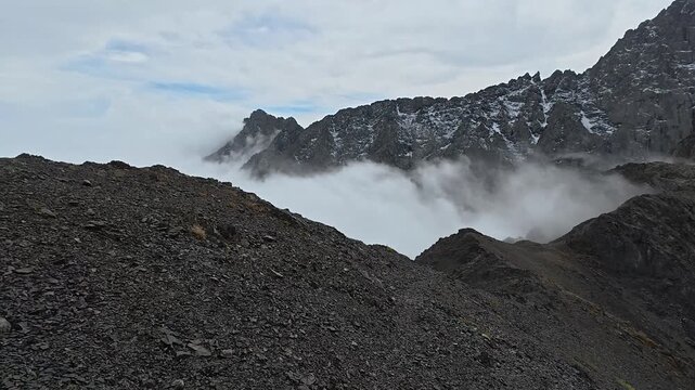 4K First-person view along a rocky ridge as clouds roll below the jagged, snow-streaked spires of Chaukhi Massif, Kazbegi, Georgia.